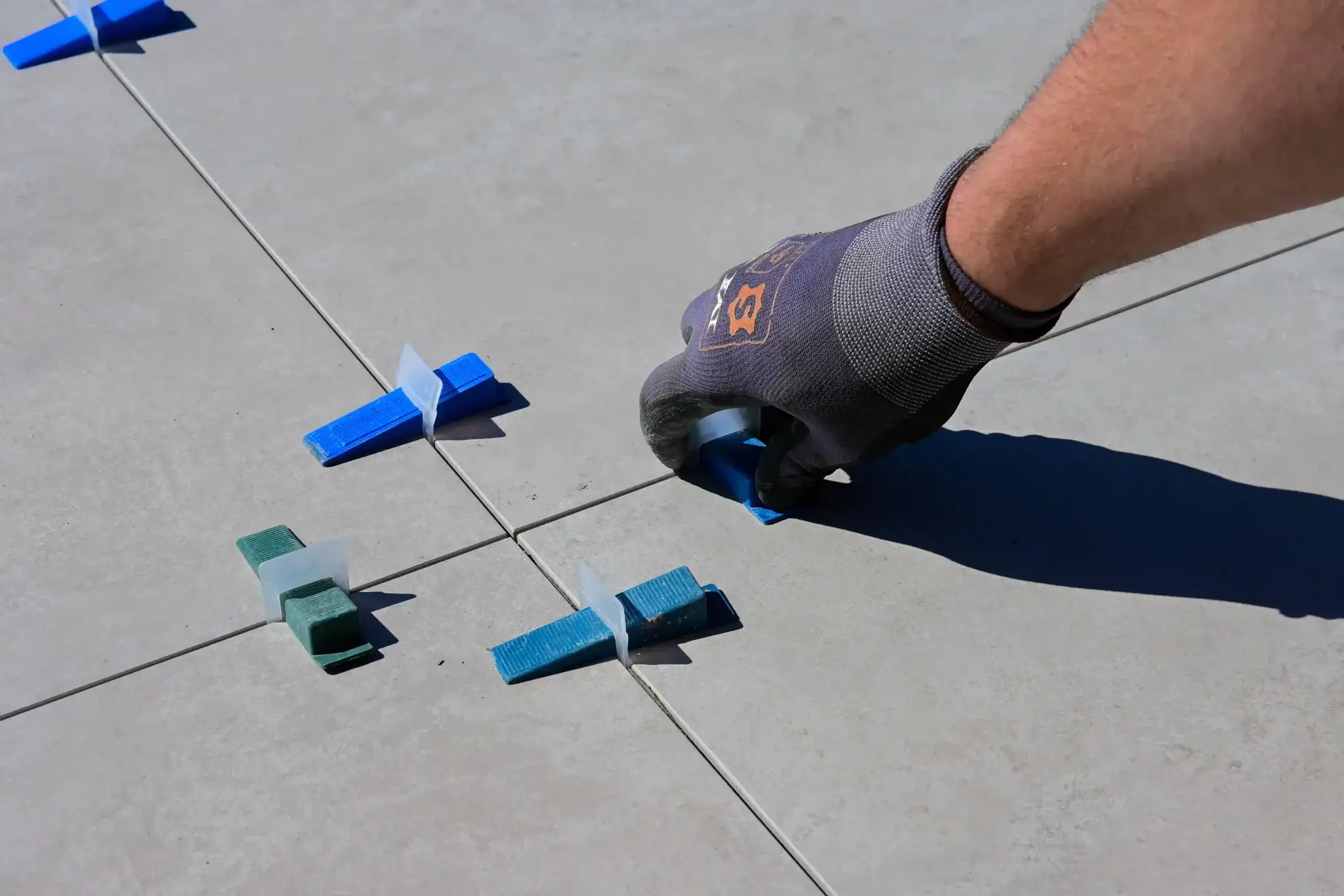 Tile installer using blue leveling clips and wedges to align large outdoor porcelain tiles