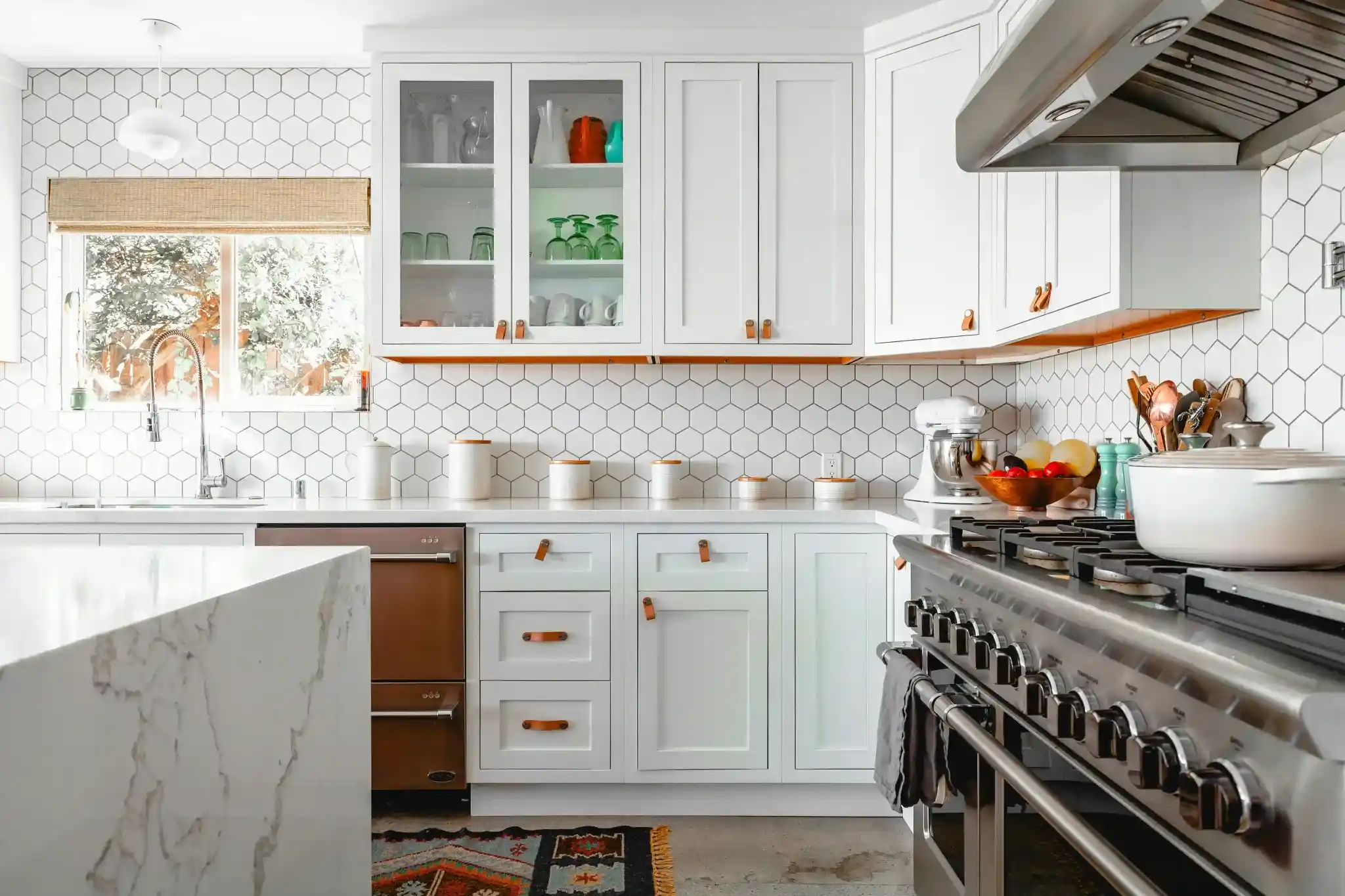 Wide view of white shaker kitchen with hexagon tile backsplash and stainless range hood