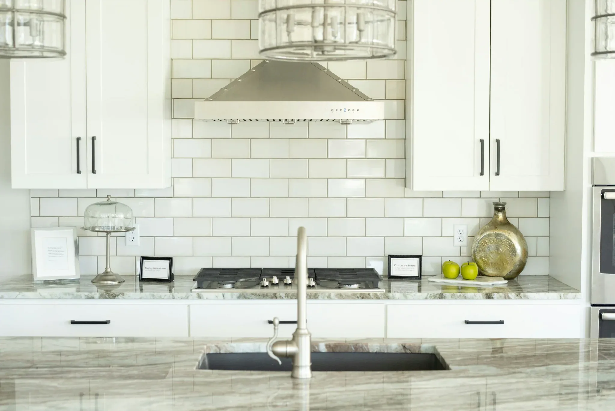 Glossy white subway tile backsplash above a kitchen sink with a small cactus and Aesop soap